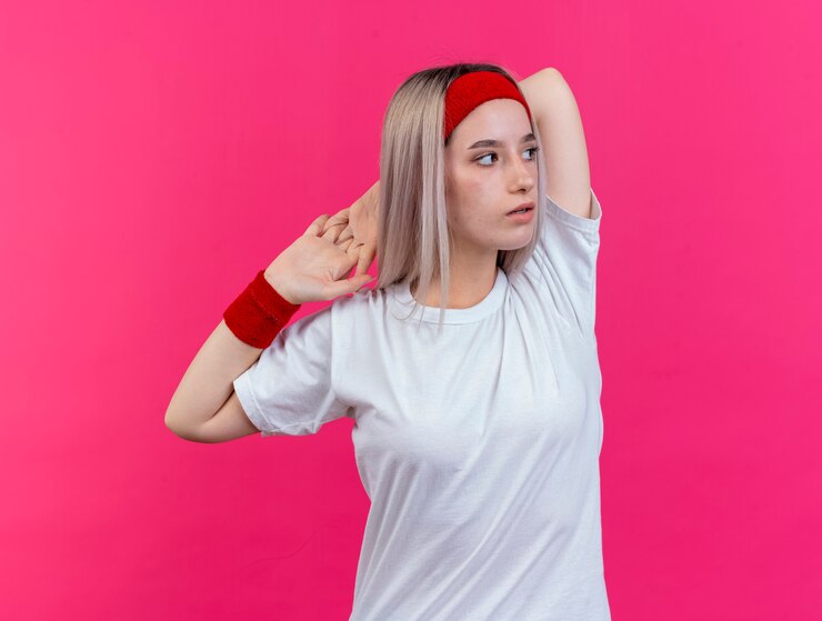 Ücretsiz Fotoğraf confident young sporty woman with braces wearing headband and wristbands holds hands together behind neck looking at side isolated on pink wall