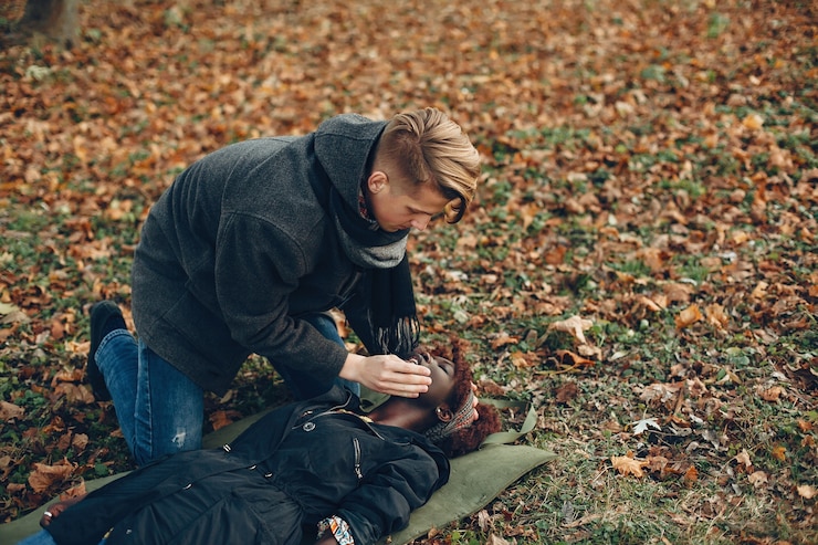 Ücretsiz Fotoğraf guy help a woman. afro girl is lying unconscious. providing first aid in the park