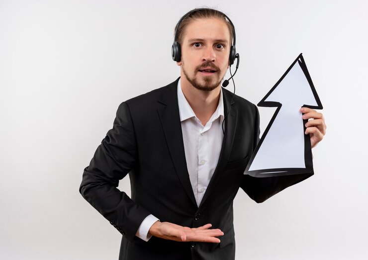 Ücretsiz Fotoğraf handsome businessman in suit and headphones with a microphone holding white arrow looking at camera confused standing over white background