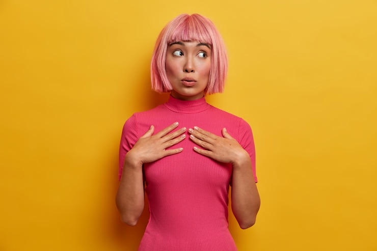 Ücretsiz Fotoğraf human emotions, reaction and attitude concept. beautiful pink haired young woman keeps hands on chest and looks with wondered expression aside