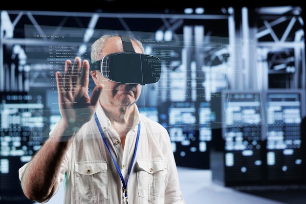 Octogenarian manager immersed in virtual reality at data center, doing equipment maintenance. Supervisor using VR headset to optimize server system performance, checking code lines