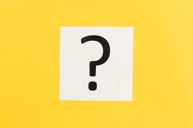 question mark on white paper on yellow background flat lay