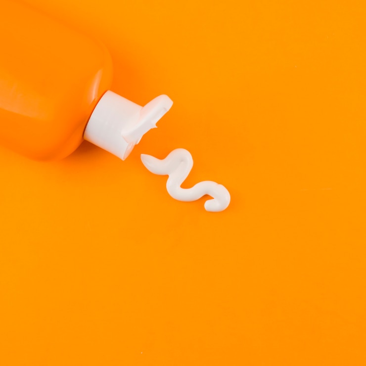 Ücretsiz Fotoğraf white sunscreen cream coming out of orange bottle against an orange backdrop
