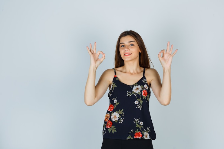 Ücretsiz Fotoğraf young woman in floral top showing ok gesture and looking cute