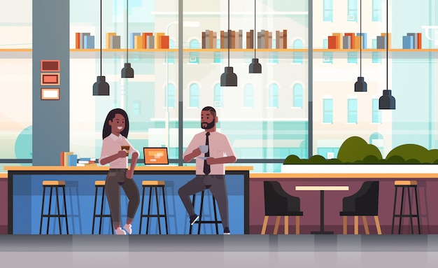 Couple assis sur une chaise au comptoir avec ordinateur portable concept de pause-café homme femme buvant du cappuccino lors de la réunion du café moderne intérieur pleine longueur horizontale