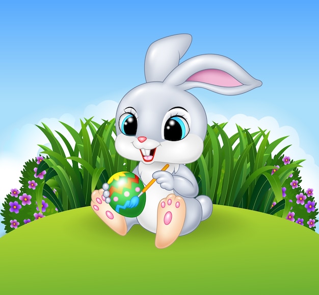 Cute Easter Bunny peignant un oeuf sur le fond de Meadow