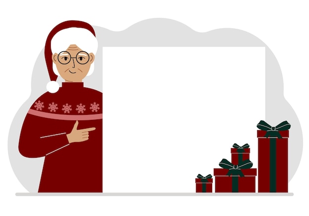 Une vieille femme en pull de Noël ou du Nouvel An avec une casquette rouge sana pointe son doigt vers une bannière une affiche vierge ou une grande feuille de papier blanche avec un espace pour le texte