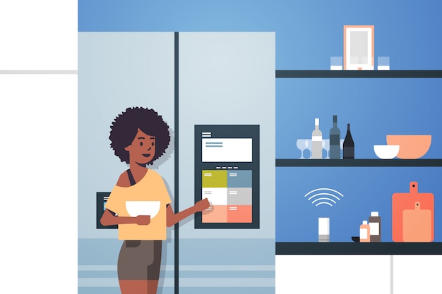 african american woman touching refrigerator screen with smart speaker voice recognition