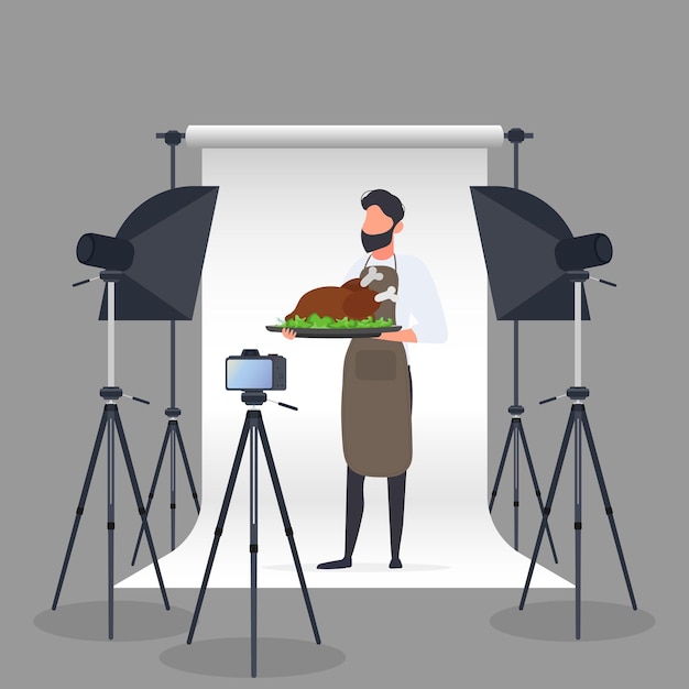Bloguero culinario. un hombre con un delantal de cocina sostiene un pollo frito en una bandeja. cámara sobre trípode, softbox. blog culinario o concepto de vlog. vector.