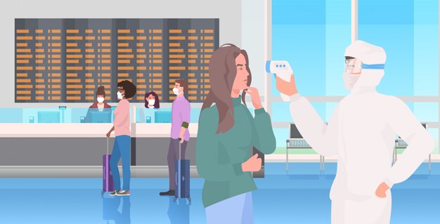 especialista en traje de materiales peligrosos que verifica la temperatura de los pasajeros en la pandemia de coronavirus de la terminal del aeropuerto