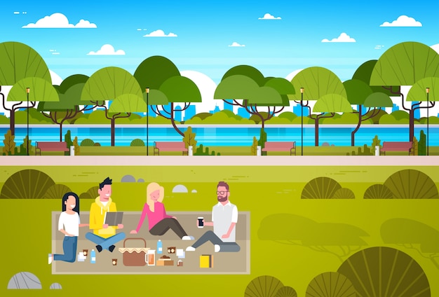 Gente feliz haciendo picnic en el parque Grupo de hombres y mujeres jóvenes sentados en el pasto relajante