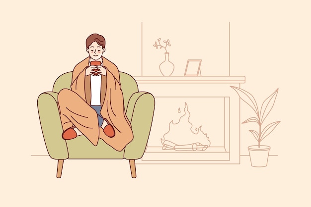 El hombre siente comodidad y armonía sentado junto a la chimenea con una manta en los hombros y una taza de café caliente