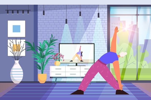 Mujer mayor haciendo ejercicios de fitness de yoga viendo tutoriales en tv formación online estilo de vida saludable vejez activa