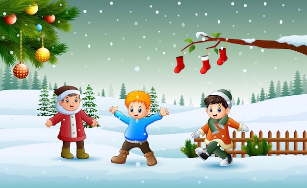 Niños felices que llevan los chlotes de un invierno que juegan en la nieve en el día de Navidad