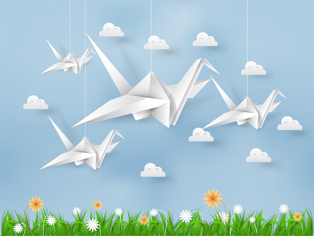Pájaros de origami volando en el cielo azul sobre campo de hierbas y flores
