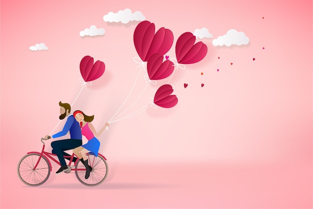 La pareja feliz está montando una bicicleta junto y sosteniendo los globos rojos en fondo rosado