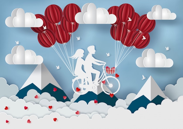 Pareja montando una bicicleta con globos rojos sobre las montañas