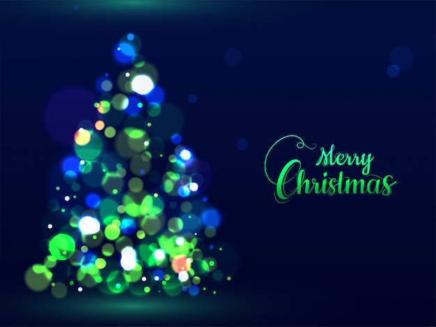 Texto de caligrafía verde feliz navidad y árbol de navidad creativo hecho por efecto bokeh en tarjeta de felicitación azul.