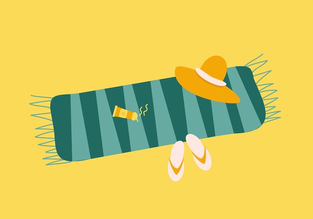Towel with sunscreen straw hat and flip flops on sand