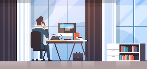 Geschaftsmann Sitzt Am Arbeitsplatz Schreibtisch Ruckansicht Geschaftsmann Mit Computer Beim Sprechen Auf Festnetz Telefon Arbeitsprozess Kreative Buro Interieur Premium Vektor