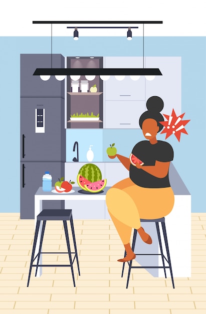 Fette fettleibige frau, die wassermelone und apfel frisches obst diät afroamerikanermädchen gesunde ernährung gewichtsverlust konzept moderne küche interieur vertikale volle länge isst