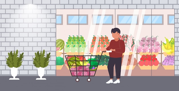 Mann kunde schieben wagen mit lebensmitteln gemüse und obst einkaufskonzept moderne lebensmittelgeschäft supermarkt außen in voller länge horizontal