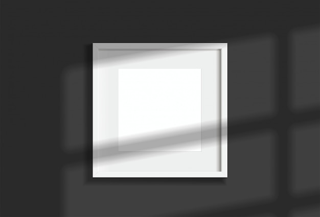 Minimales leeres quadratisches weißes Rahmenbild, das an dunkler Wand mit Fensterlicht und Schatten hängt. Abbildung isolieren.