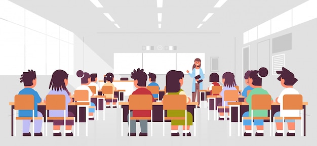 Schülergruppe sitzt und hört der Lehrerin im Klassenzimmer während des Unterrichtsunterrichtskonzeptes des modernen Klassenzimmerinnenraums zu