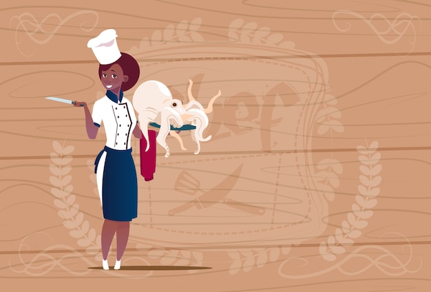 Weiblicher afroamerikaner-chef cook holding octopus cartoon-chef in der restaurant-uniform über hölzernem strukturiertem hintergrund