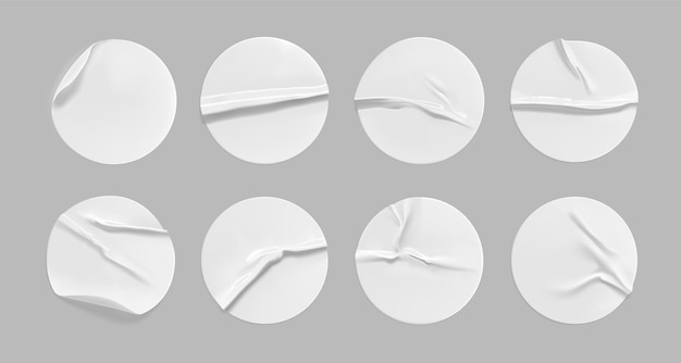 Weißes rundes zerknittertes Aufkleberset. Selbstklebendes weißes Papier- oder Plastikaufkleberetikett mit geklebtem, faltigem Effekt auf grauem Hintergrund. Leere Vorlagen eines Etiketts oder Preisschilder. 3D realistisch.