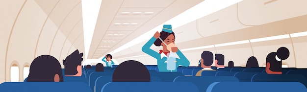 Aeromoça explicando para os passageiros como usar a máscara de oxigênio em situação de emergência afro-americano aeromoça conceito de demonstração segurança moderna placa de avião interior horizontal
