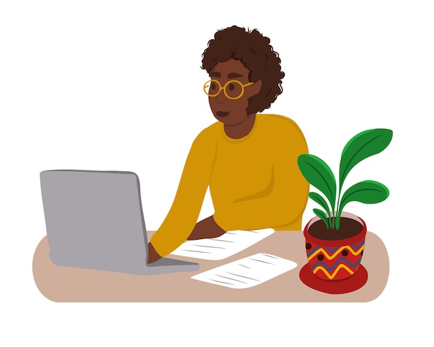 Uma mulher afro-americana se senta em uma mesa com um laptop e lê um documento na mesa
