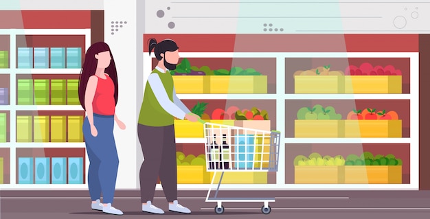 Coppia spingendo carrello carrello con generi alimentari sovrappeso uomo donna shopping insieme obesità stile di vita malsano concetto moderno negozio di alimentari interno a figura intera piatta orizzontale