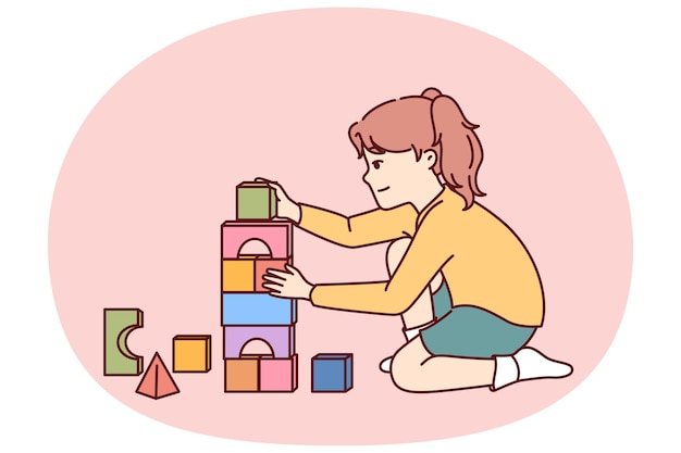 La bambina gioca seduta sul pavimento e costruisce una torre di mattoni giocattolo per il concetto di giochi educativi