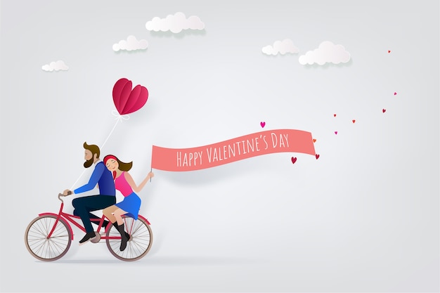 La coppia felice sta guidando una bicicletta insieme e sta tenendo il nastro rosa felice di San Valentino