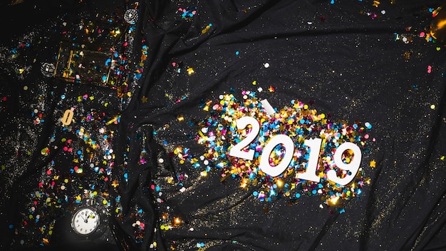 Gratis foto 2019 heldere cijfers tussen confetti op donkere doek