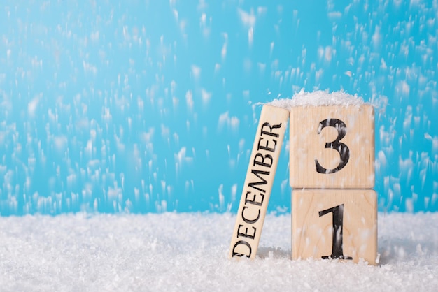 2021 komt eraan. close-up foto van houten kubus kalender met de laatste dag van het oude jaar op sneeuw vallende achtergrond en blauwe heldere kleur hemelachtergrond