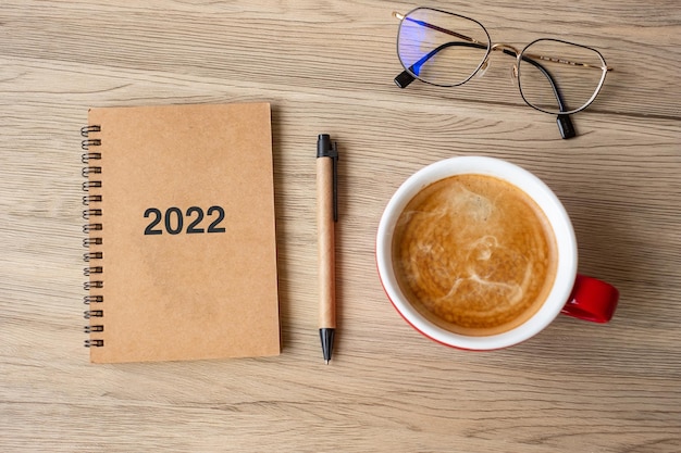 2022 notebook en koffiekopje op houten tafel, bovenaanzicht en kopieer ruimte. kerstmis, gelukkig nieuwjaar, doelen, resolutie, takenlijst, strategie en planconcept