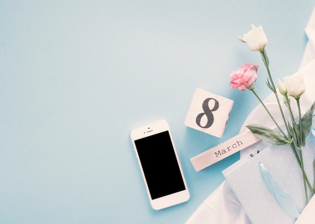 Gratis foto 8 maart inscriptie met bloemen en smartphone op tafel