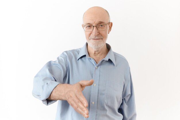 Aangenaam kennis te maken. Geïsoleerde shot van elegante formeel geklede oudere man met witte baard die handpalm reikt en je hand gaat schudden als teken van begroeting. Lichaamstaal, tekens en gebaren