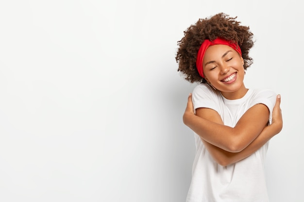 Aangenaam uitziende vrouw knuffelt zichzelf, herinnert zich een romantisch moment met vriend, houdt het hoofd schuin en sluit de ogen met plezier