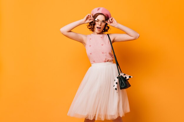 Aangename krullende vrouw die in glazen camera bekijkt. studio shot van frans vrouwelijk model poseren op gele achtergrond.