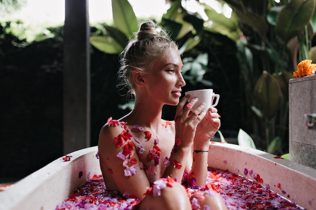 Aangename vrouw zittend in Bad op natuur achtergrond en glimlachen. Schattige blonde vrouw thee drinken tijdens spa in weekend.