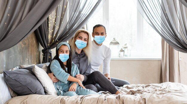 Aanhankelijke jonge moeder die dochtertje omhelst, familie die een medisch gezichtsmasker draagt, steun geeft, troost, liefde uitdrukt. Concept van coronavirus of COVID-19 pandemische ziektesymptomen.