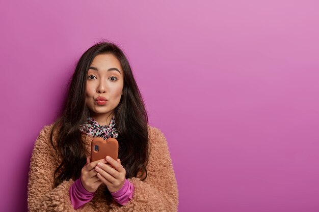 Aanhankelijke vrouw met natuurlijk steil haar houdt de lippen rond, bekijkt video online, stuurt berichten in online chat
