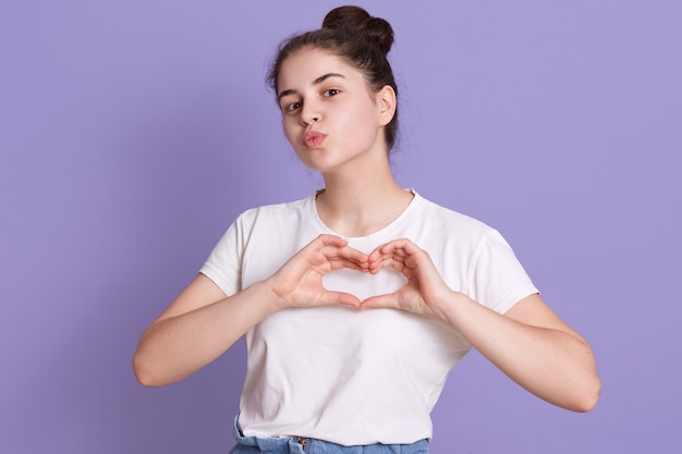 Aantrekkelijk donkerbruin wijfje dat witte toevallige t-shirt draagt die hartgebaar maakt