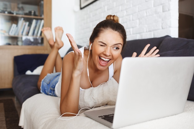 Aantrekkelijk jong meisje dat op bank bij woonkamer met laptop legt.