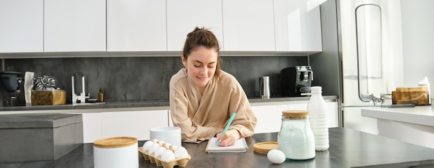 Gratis foto aantrekkelijk jong vrolijk meisje bakken in de keuken het maken van deeg met receptboek met ideeën