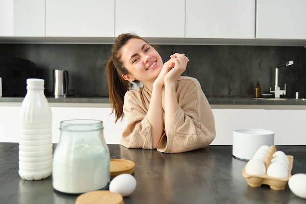 Gratis foto aantrekkelijk jong vrolijk meisje dat in de keuken bakt en deeg maakt met receptenboek met ideeën