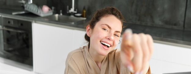 Aantrekkelijk jong vrolijk meisje dat in de keuken bakt en deeg maakt met receptenboek met ideeën